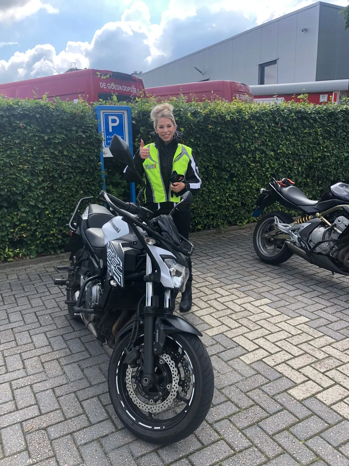 Leerling steekt haar duim op naast een Kawasaki-lesmotor, in YesMotor-hesje